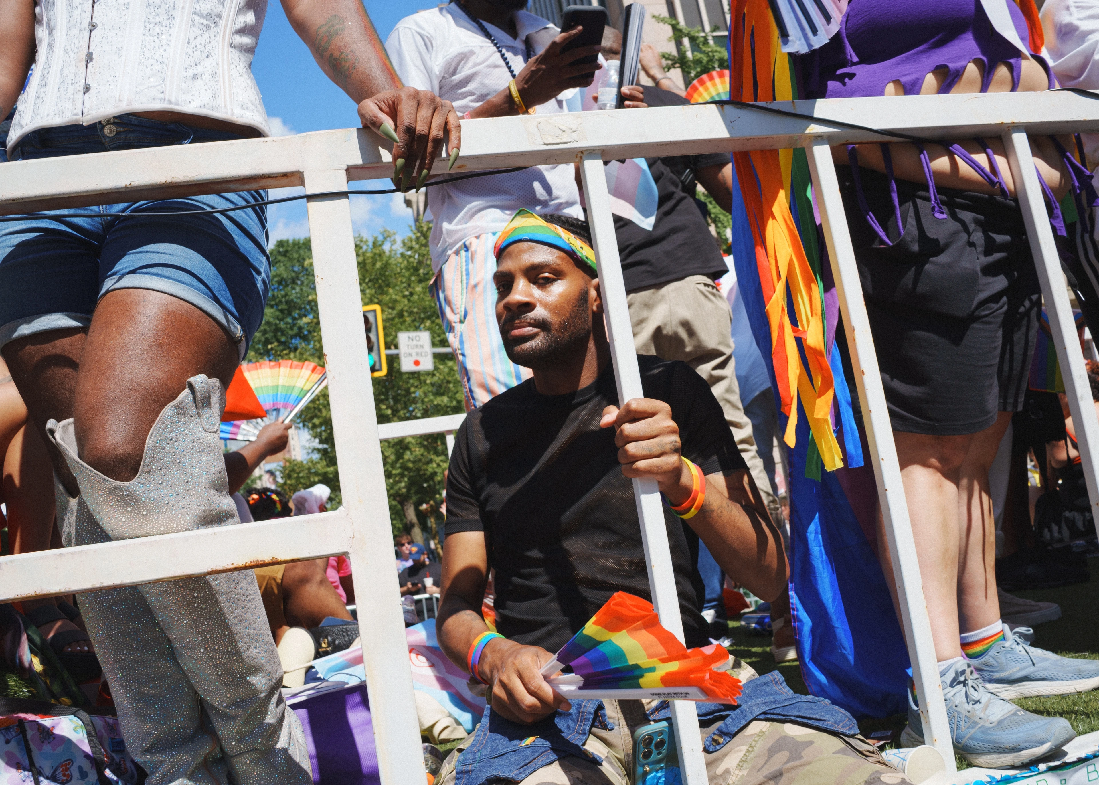 A bearded man sits behind a white metal crowd-control barricade, gripping one bar, at a public gathering, Washington, D.C.